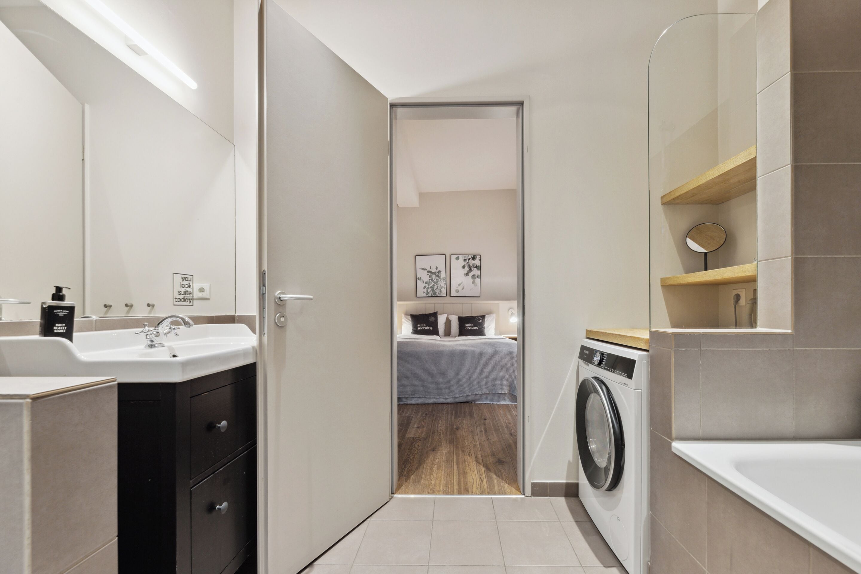 A modern bathroom with a sink, mirror, and a washing machine.