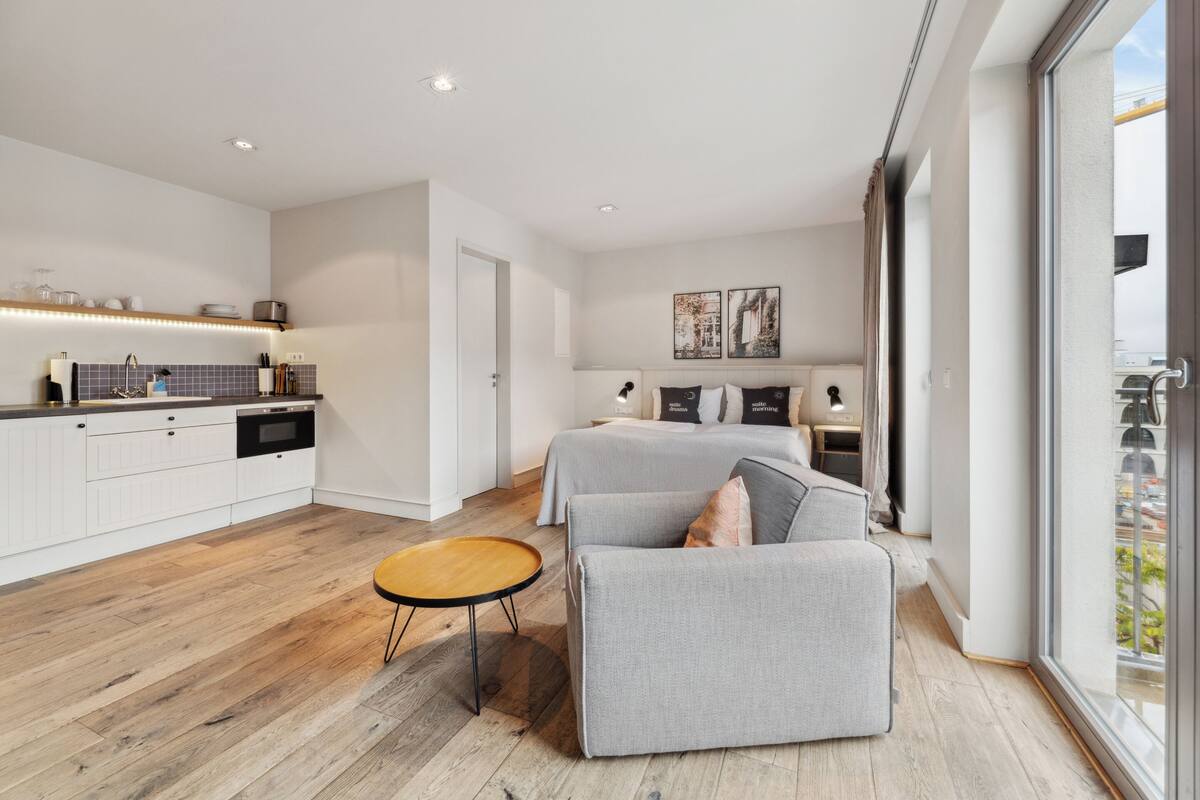 Une chambre d’hôtel moderne dotée d’une kitchenette, d’un grand lit, d’un coin salon et offrant une vue sur la ville.