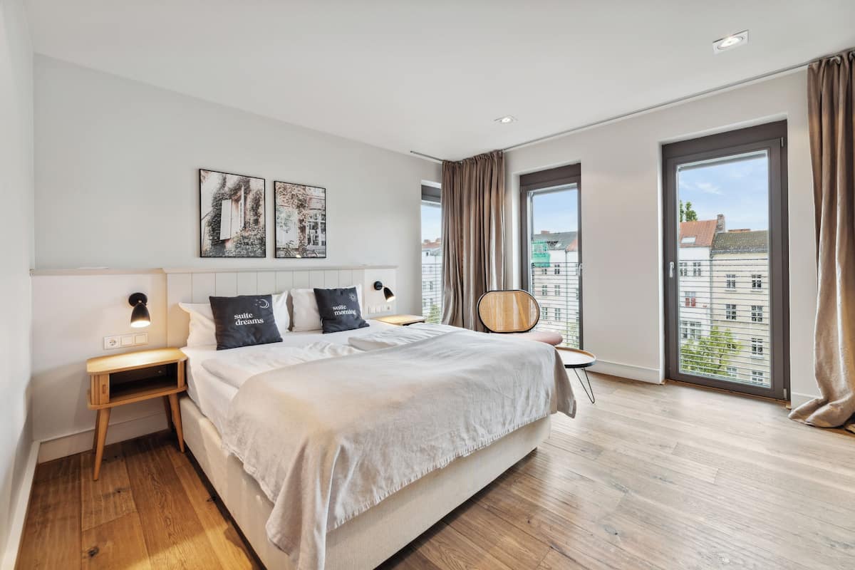 Une chambre d’hôtel moderne, dotée d’un grand lit, d’une table de chevet, d’une chaise et offrant une vue sur la ville grâce à de grandes fenêtres.