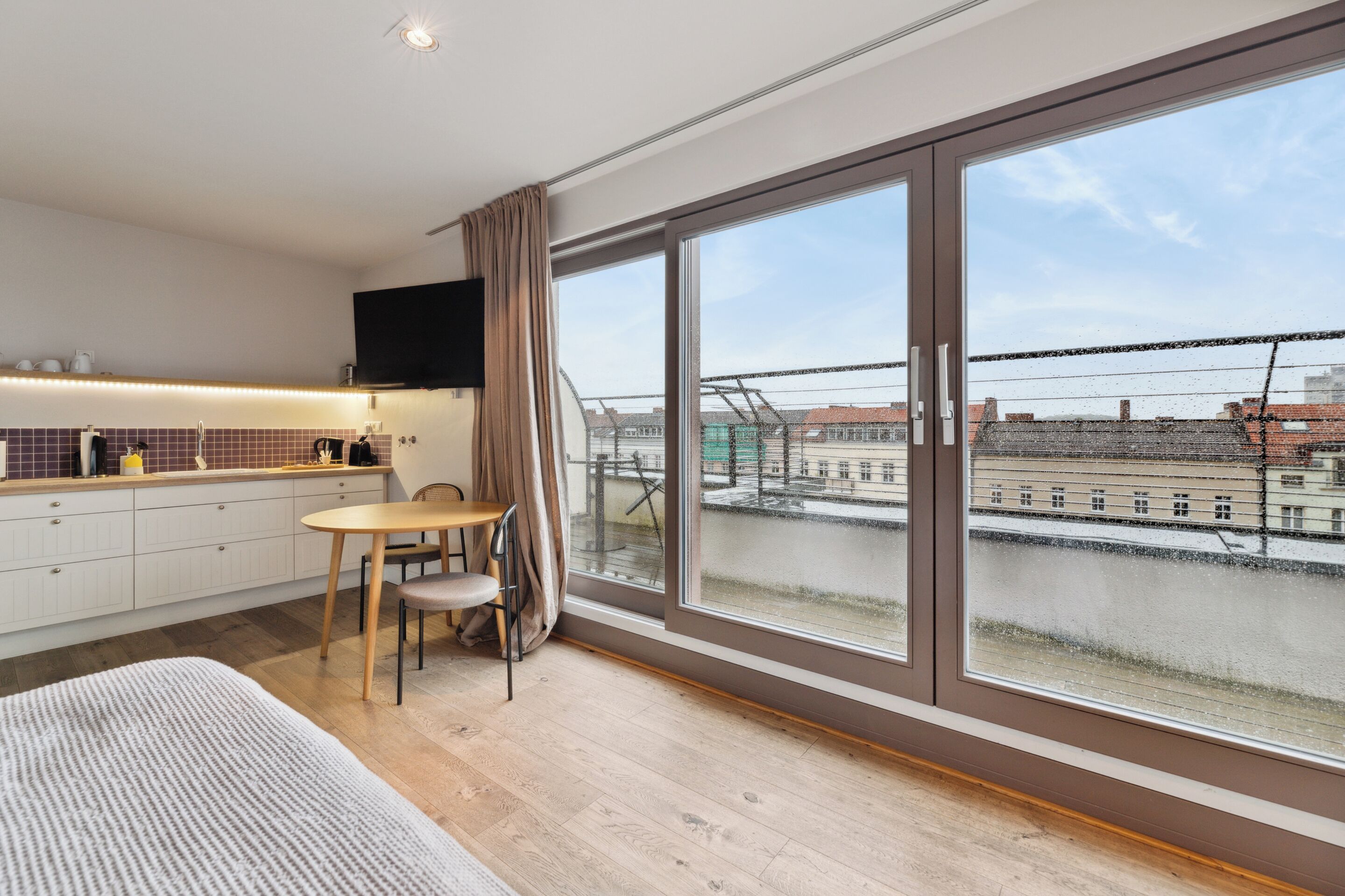 A modern kitchen with a dining area, large windows, and a city view.