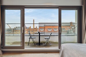 Een balkon met een tafel en stoelen, met uitzicht op gebouwen en een schoorsteen op de achtergrond.