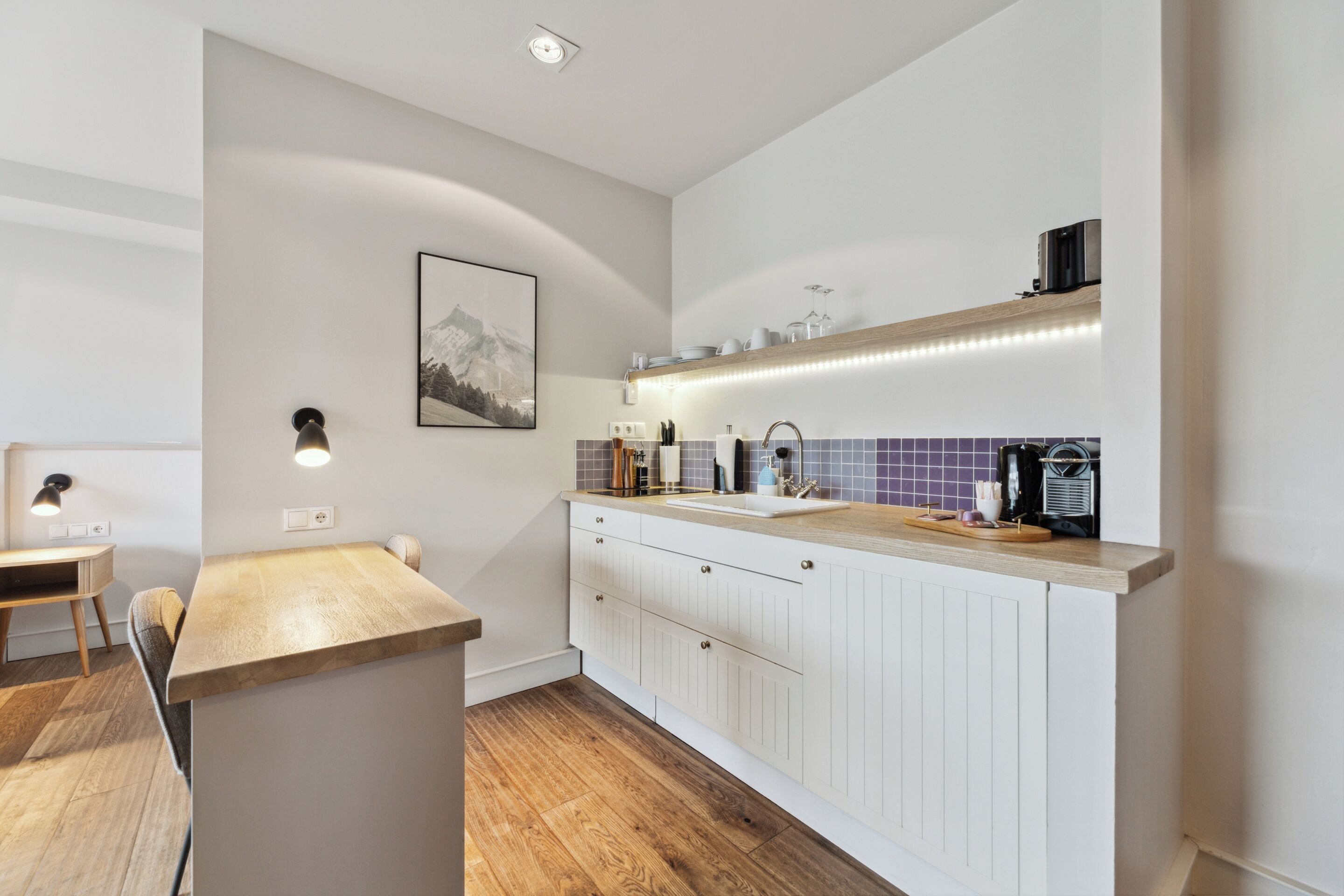 A modern kitchen with a wooden countertop, white cabinets, and a tiled backsplash.