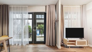 Een moderne woonkamer met houten vloer, een televisie op een houten standaard, en een zithoek met een tafel en stoel.