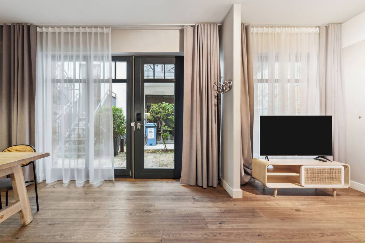 Un salon moderne avec un plancher en bois, un téléviseur posé sur un meuble en bois, et un coin repas comprenant une table et des chaises.