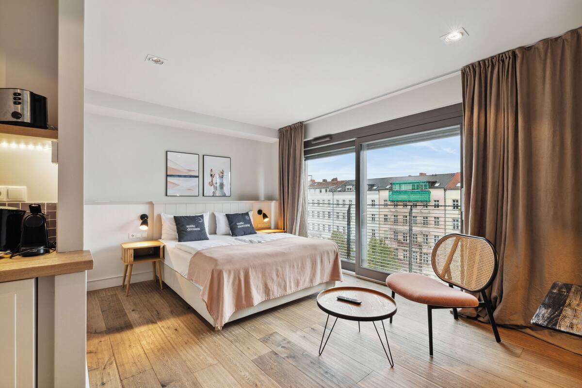 Une chambre d’hôtel moderne avec un grand lit, un petit bureau, une chaise et une vue sur la ville grâce à de grandes fenêtres.