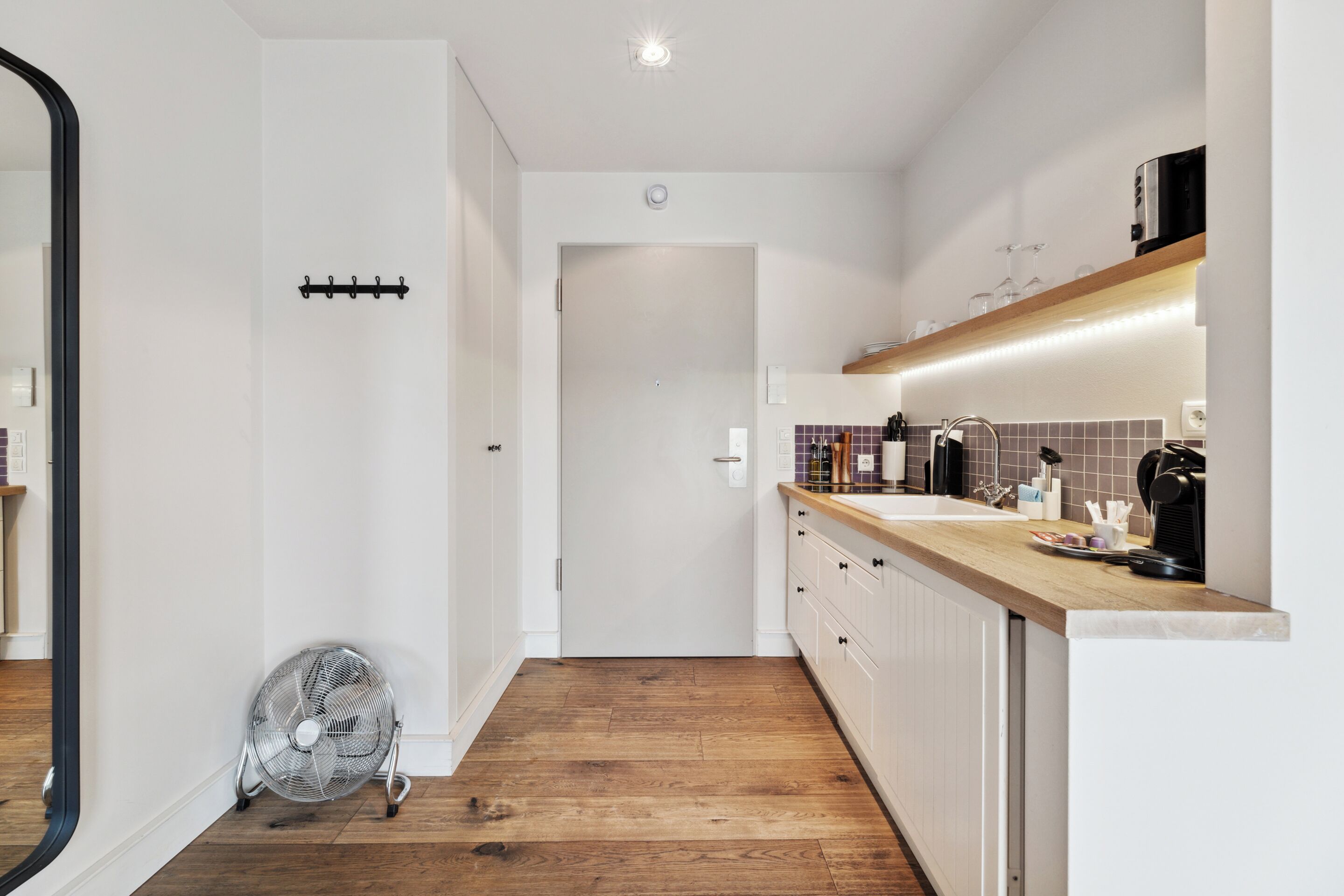 A modern kitchen with wooden flooring, white cabinets, and a built-in oven.
