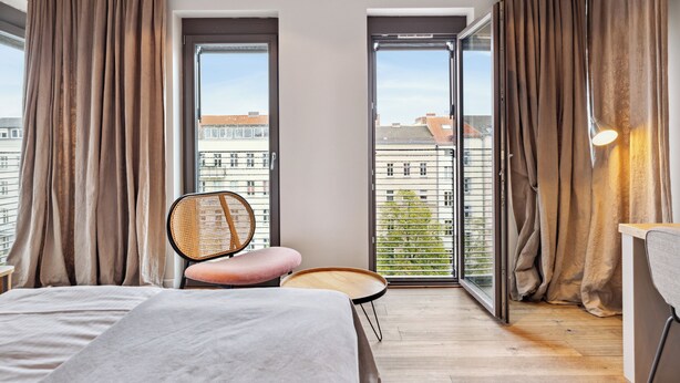 Een moderne slaapkamer met een groot bed, een stoel, een klein tafeltje en een balkon met gordijnen.