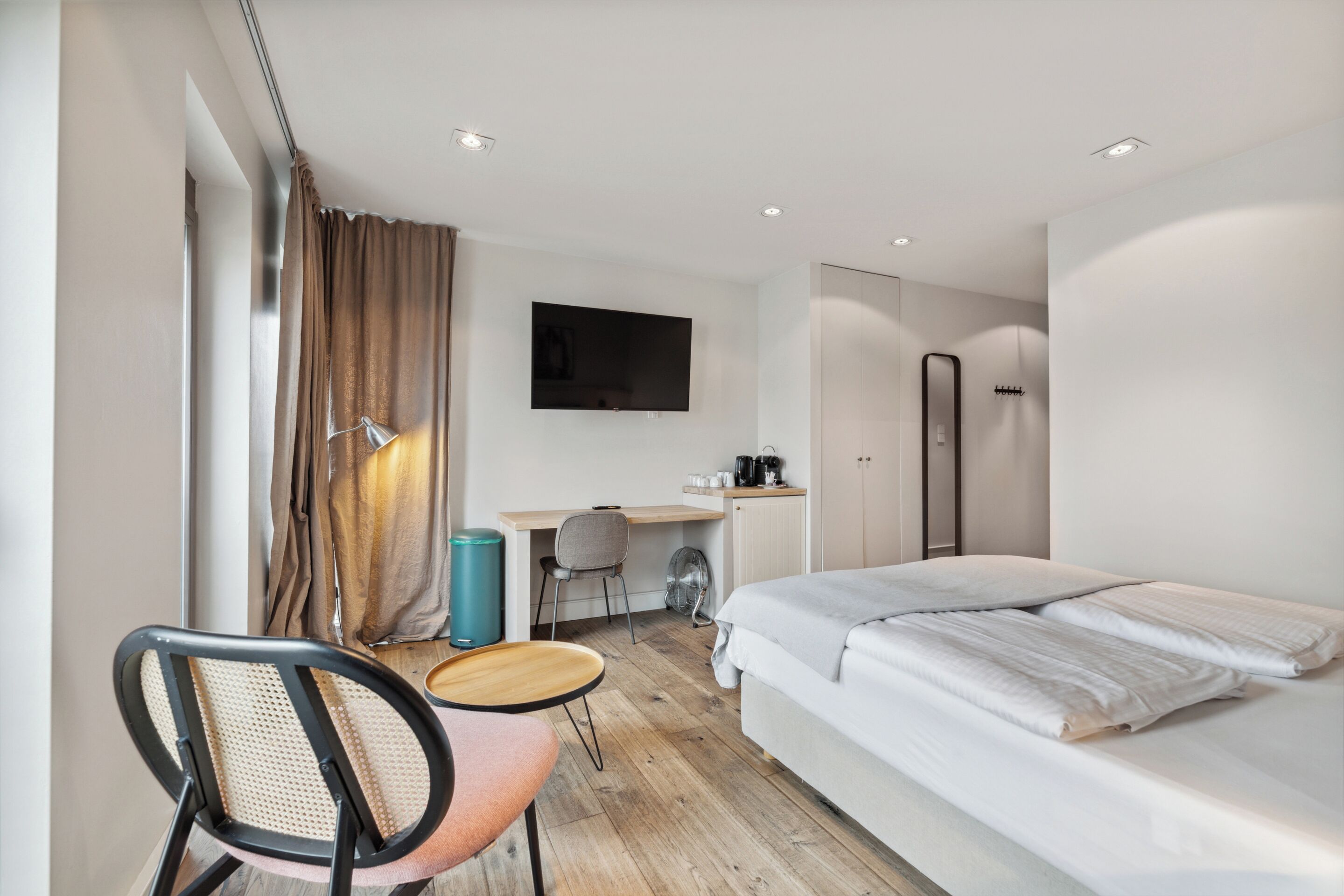 A modern hotel room with a bed, desk, chair, and a TV mounted on the wall.