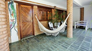 A hammock chair in a covered outdoor area with brick pillars, wooden doors, and a tiled floor. - Pousada Lua Cheia (Marechal Deodoro)