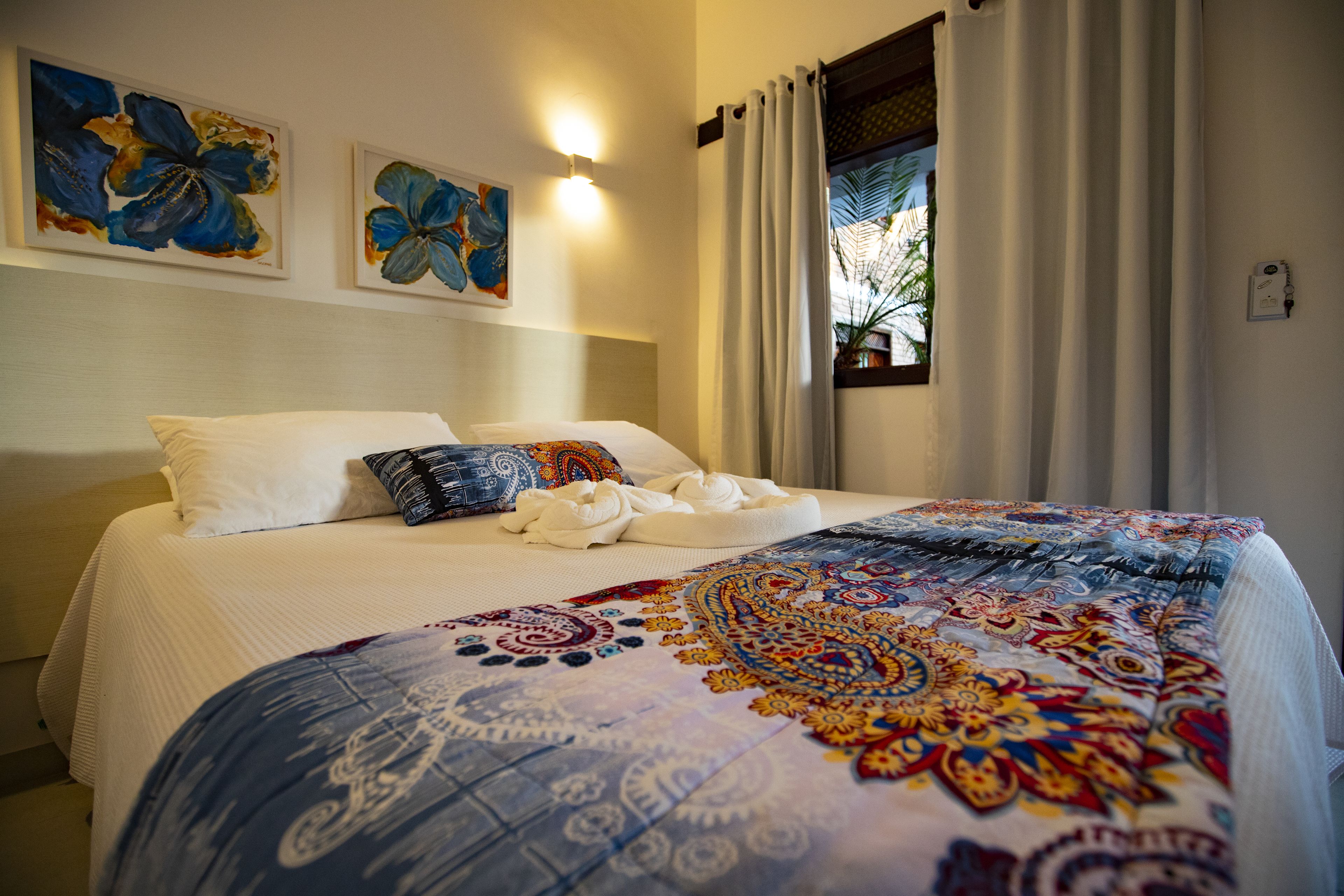 Een hotelkamer met een groot bed, twee wandlampen en twee bloemstillevens.