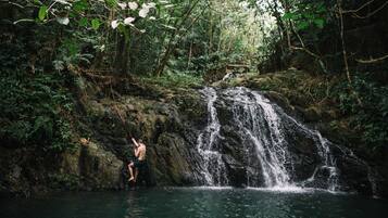 Uma cascata numa área arborizada, com uma pessoa em sua base.