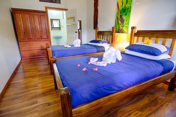 A hotel room with two wooden beds, each with a blue bedspread and white towels. - Bocawina Rainforest Resort & Adventures (Hopkins)