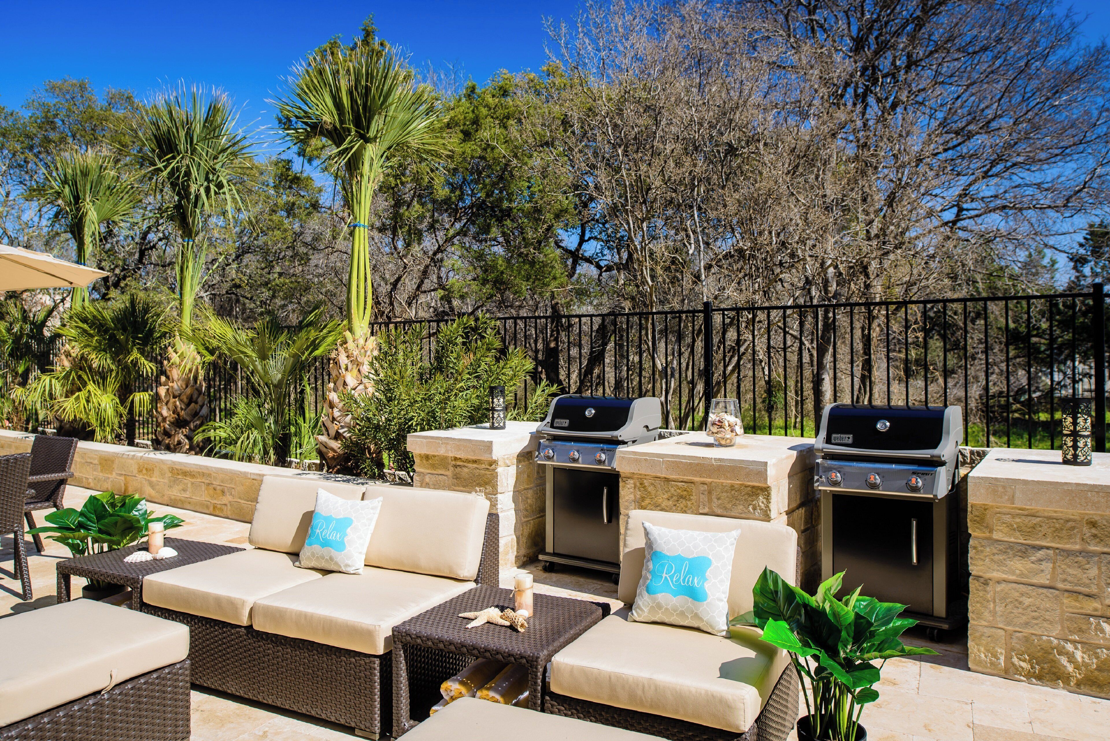 An outdoor seating area with two Weber grills, cushioned sofas, and a stone wall backdrop.