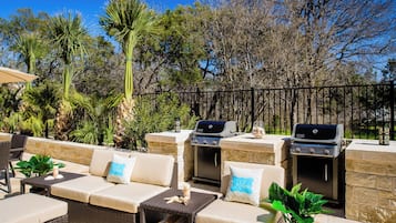 An outdoor seating area with two Weber grills, cushioned sofas, and a stone wall backdrop.
