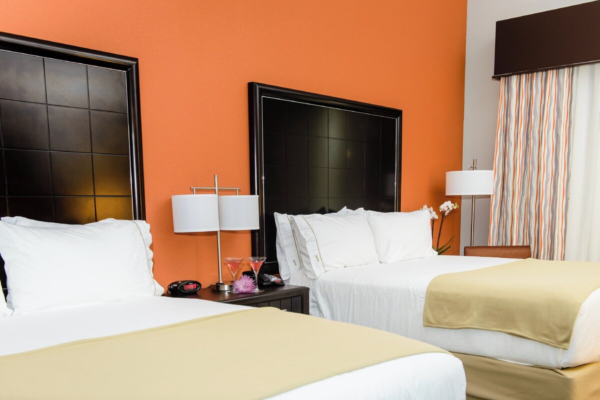 A hotel room with two beds, a nightstand with a lamp, a telephone, and a decorative item.