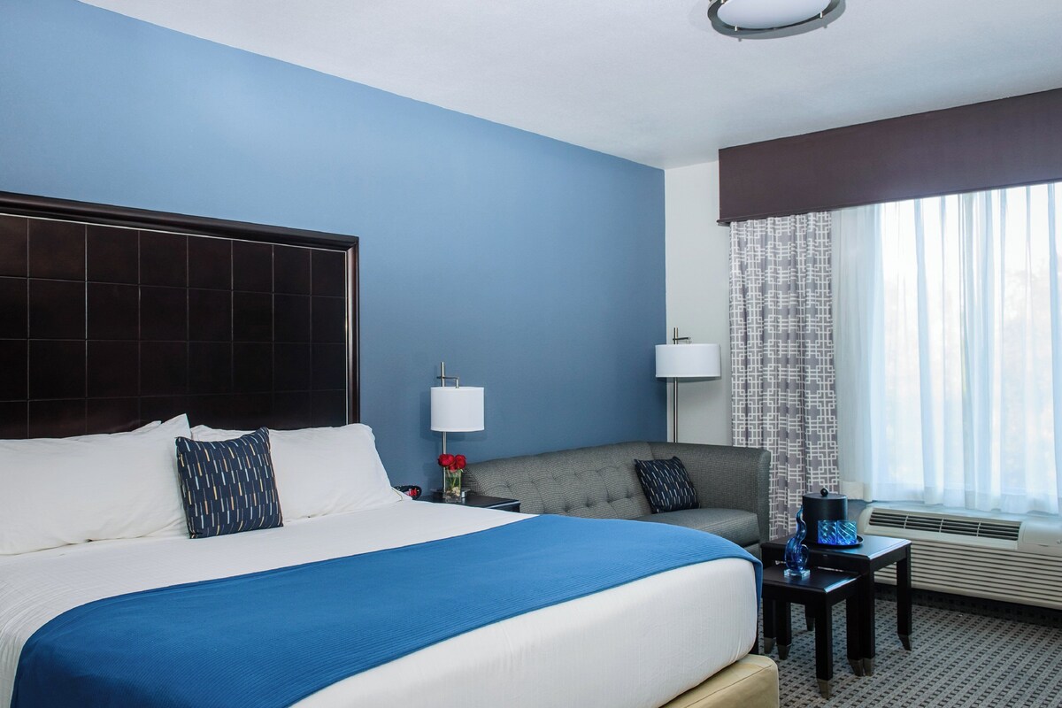 A hotel room with a large bed, a sofa, a desk, and a window with curtains.