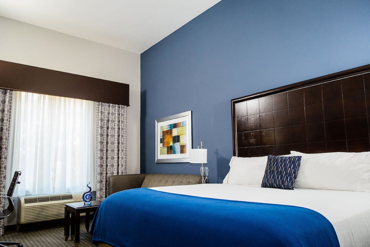 Habitación de hotel con una cama grande, un escritorio, una silla y un ventanal con cortinas.
