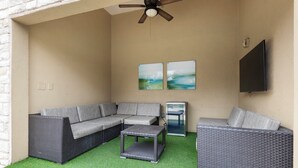 Een terras buiten met een sectiesofa, een bijzettafeltje en een flatscreen televisie aan de wand.