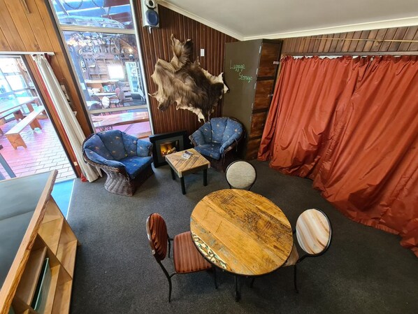 A cozy room with a fireplace, two blue armchairs, a round wooden table, and a large fur rug. - Chateau Backpacker & Motels (Franz Josef Glacier)