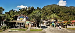 A two-story building with a sign for a motel and backpackers, surrounded by lush greenery and a mountain in the background.