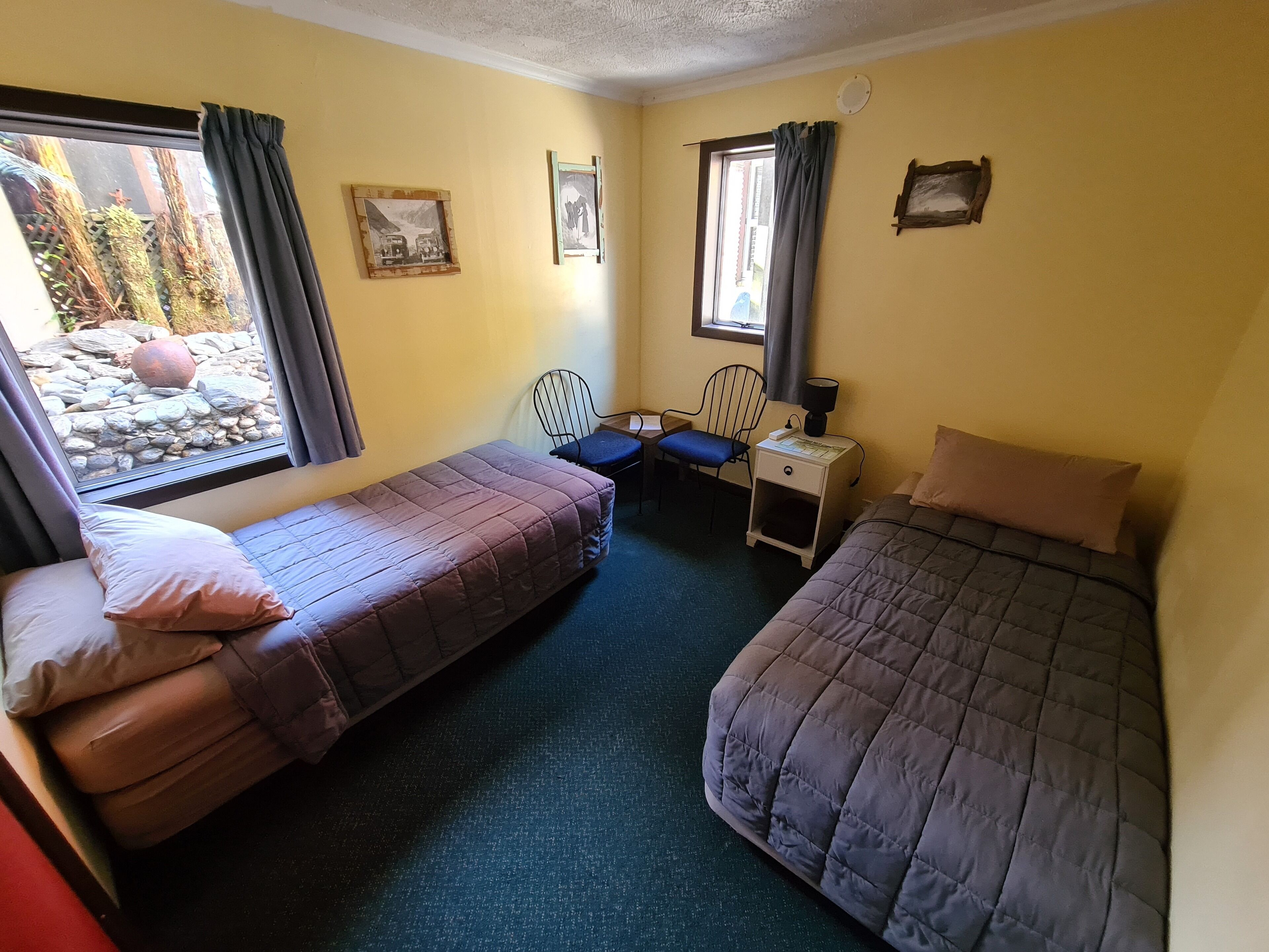 A room with two beds, a desk, a chair, and a window with curtains.