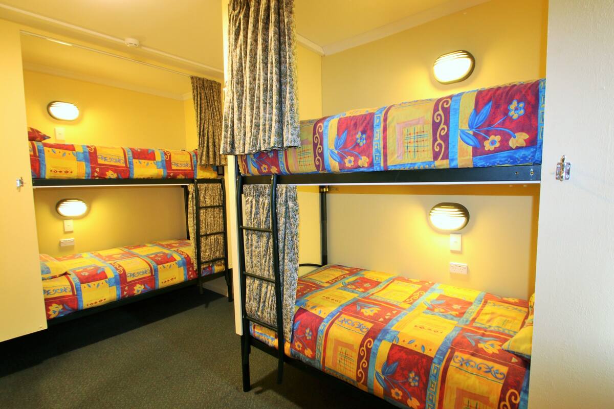 A room with bunk beds, each with a patterned bedspread and a round wall light.