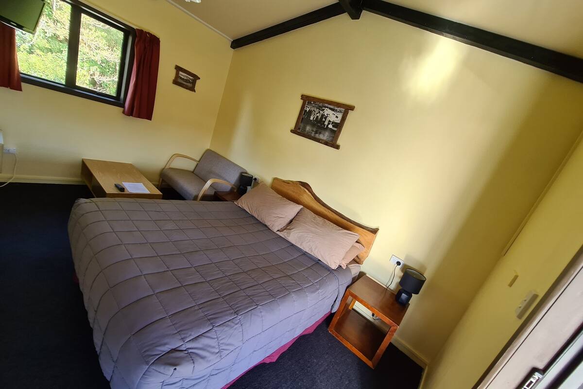 A bedroom with a large bed, a bedside table, a nightstand, a window with curtains, and a ceiling fan.