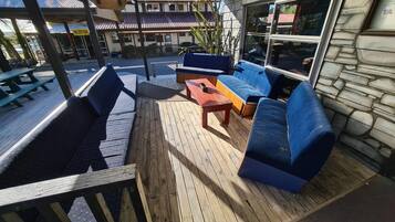 An outdoor seating area with wooden flooring, blue cushioned seating, and a stone wall.