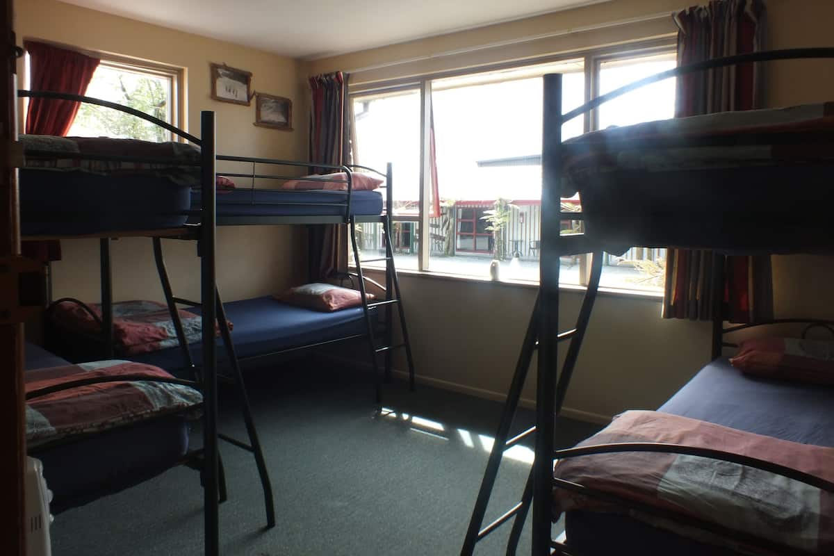 A dormitory room with bunk beds, a window with curtains, and a ceiling fan.