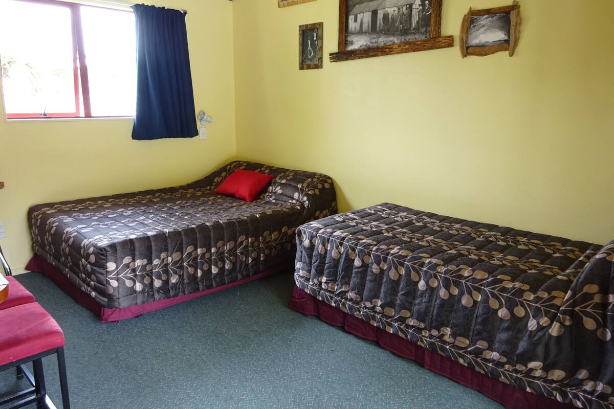 A room with two single beds, a window with curtains, and a small table with a chair.
