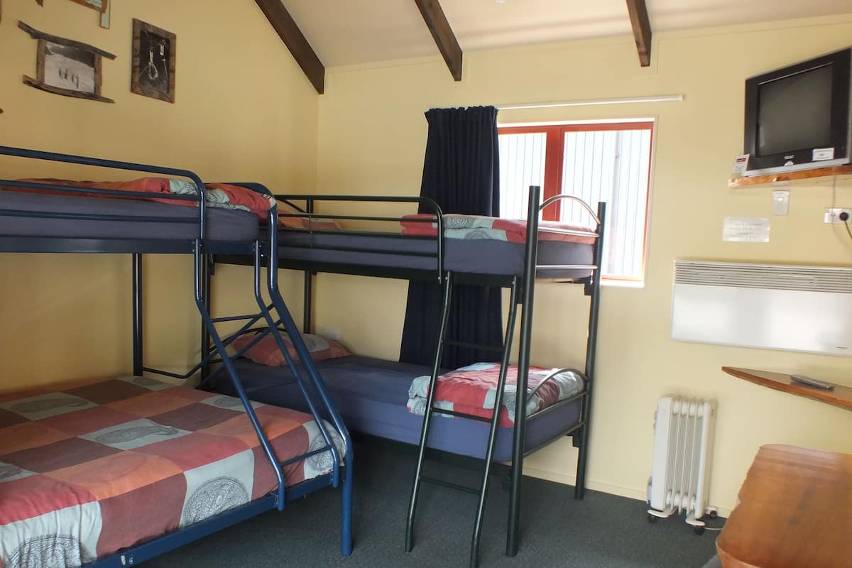 A bunk room with two bunk beds, a window with curtains, a radiator, and a television on the wall.