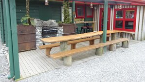 A rustic outdoor seating area with a wooden bench and a stone fireplace.