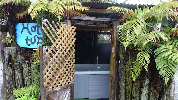 A rustic hot tub area with a wooden lattice entrance, surrounded by lush ferns and a sign indicating the temperature.