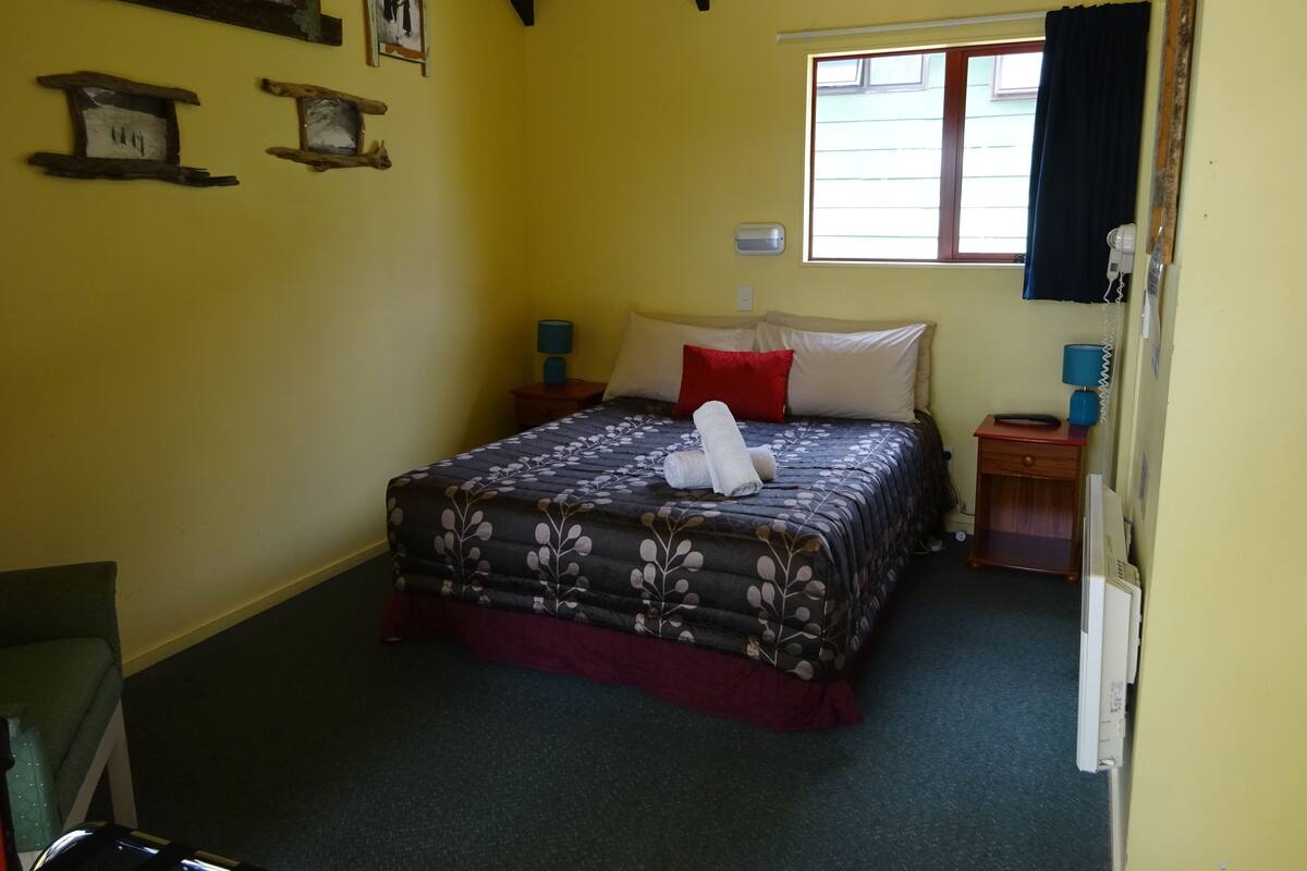 A bedroom with a bed, two bedside tables, a window, and a wall-mounted heater.