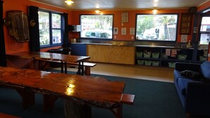 A restaurant with wooden tables and benches, a kitchen area, and large windows with a view of the outside.