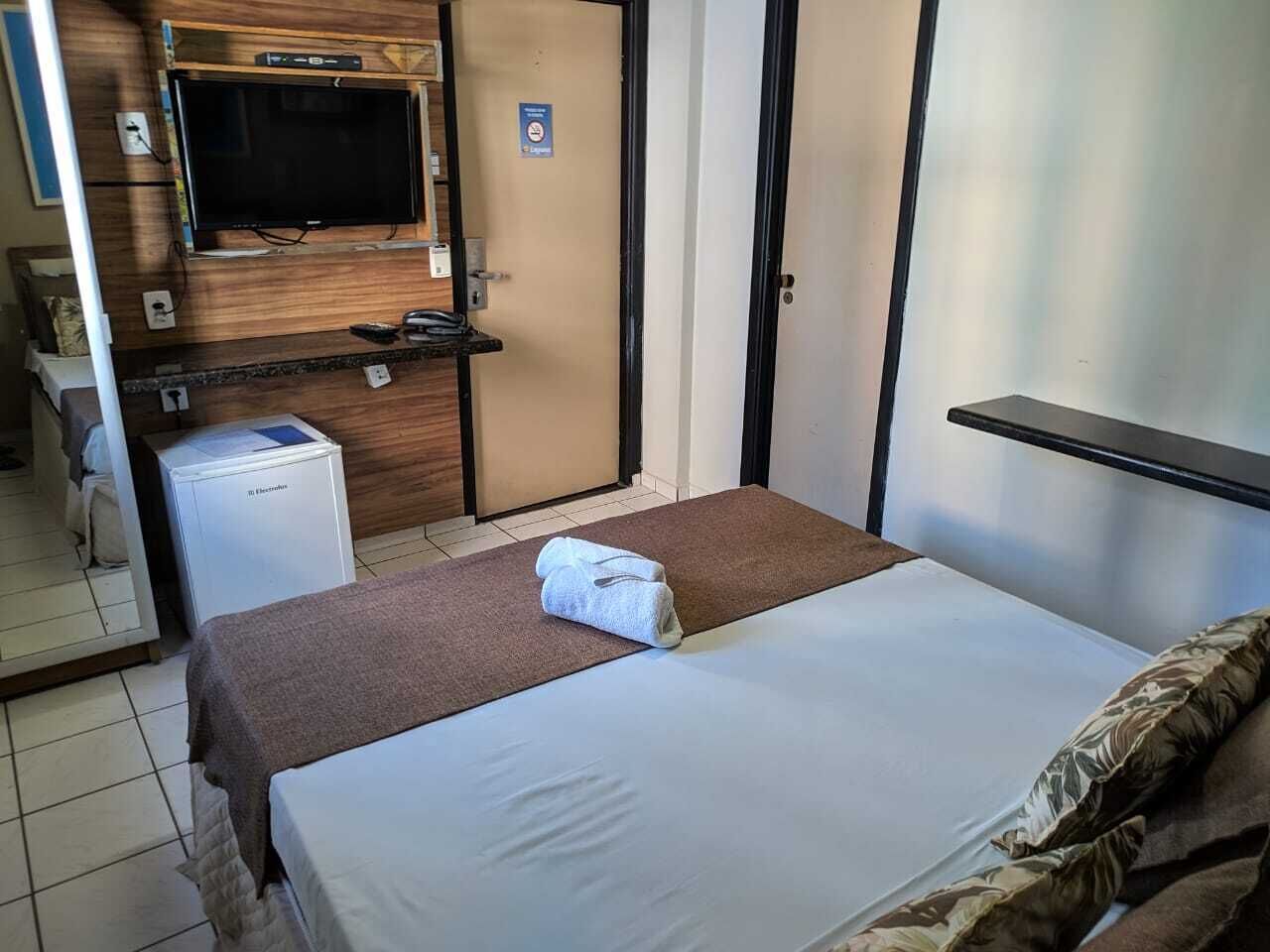 A hotel room with a bed, a television, a minibar, and a door with a sign.