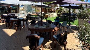 An outdoor patio with wooden tables and chairs, umbrellas, and a fire pit.