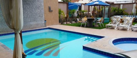 Una piscina con un logotipo azul y verde, rodeada de sillas de descanso y una mesa con sombrillas.