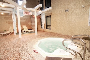 An indoor pool area with a hot tub, lounge chairs, and a warning sign.