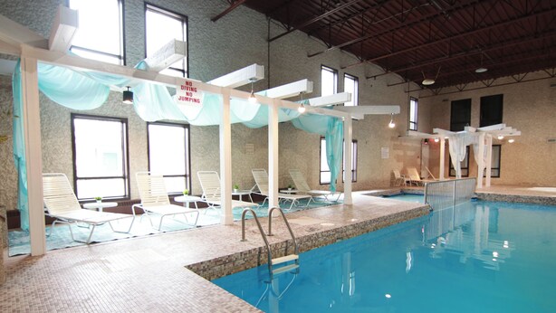 Une piscine intérieure avec un revêtement de sol carrelé, des chaises longues blanches et un escalier d’accès à la piscine.