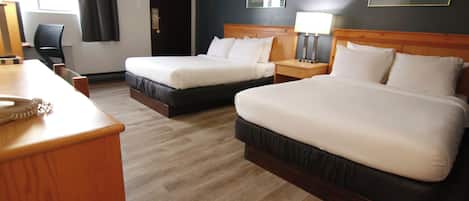 A hotel room with two beds, a wooden desk, a chair, a nightstand with a lamp, and a framed picture on the wall.