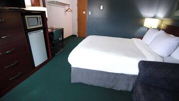 A hotel room with a bed, a desk with a telephone, a microwave, and a coat rack.