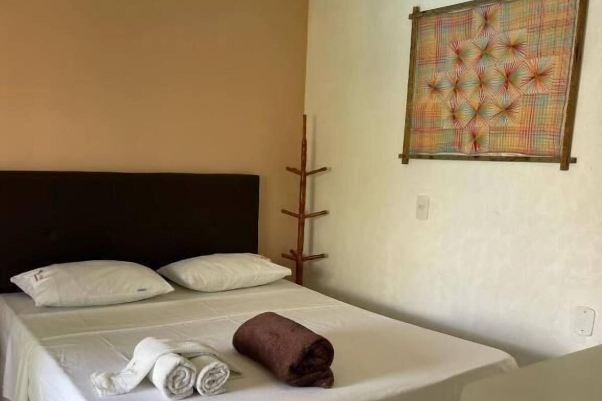 Una habitación de hotel con una cama, un perchero de madera y un cuadro en la pared.