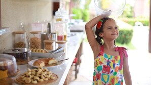 A buffet setup with various food items and a child balancing a bowl on her head.