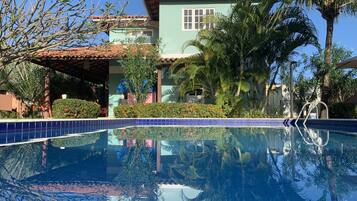 Una piscina azul cristalina con borde de azulejos, rodeada de abundante vegetación y palmeras.