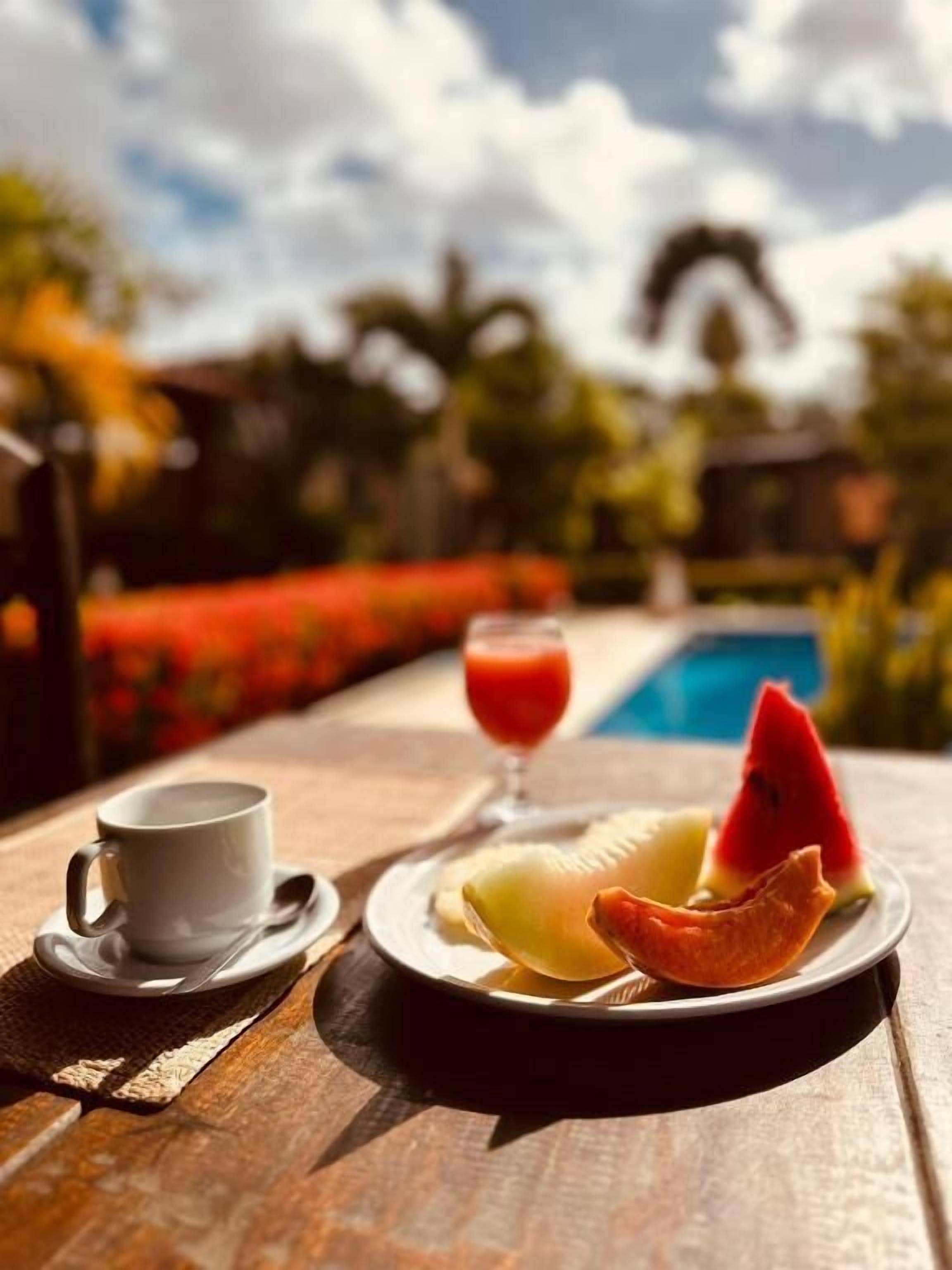 Une table en bois dressée pour le petit-déjeuner, avec une tasse, une assiette de fruits et un verre de jus.