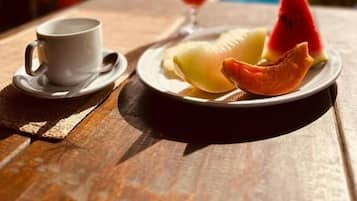 Une table en bois dressée pour le petit-déjeuner, avec une tasse, une assiette de fruits et un verre de jus.