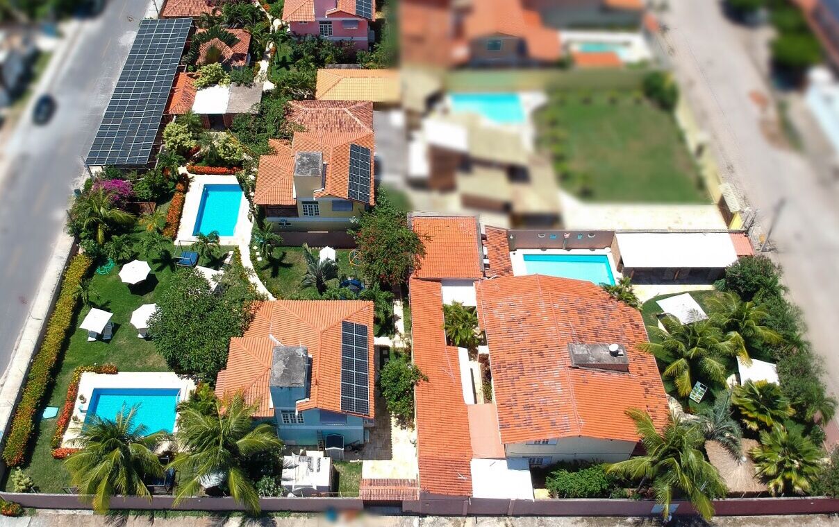 A residential area with multiple houses, solar panels, swimming pools, and palm trees.