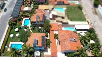 A residential area with multiple houses, solar panels, swimming pools, and palm trees.
