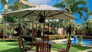 A circular wooden table with chairs and a large umbrella in a lush garden setting.